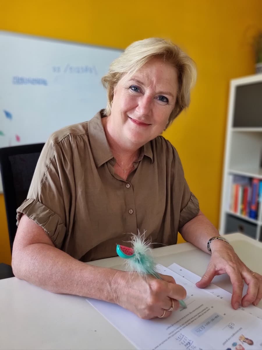 Ina Geuze-van Faassen aan haar werktafel met een pen in de hand, voor de gele wand van haar leerstudio.