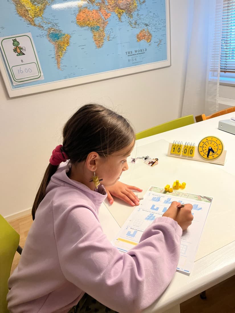 Een kind werkt aan een rekenopdracht met blokjes en een leerklok op tafel.